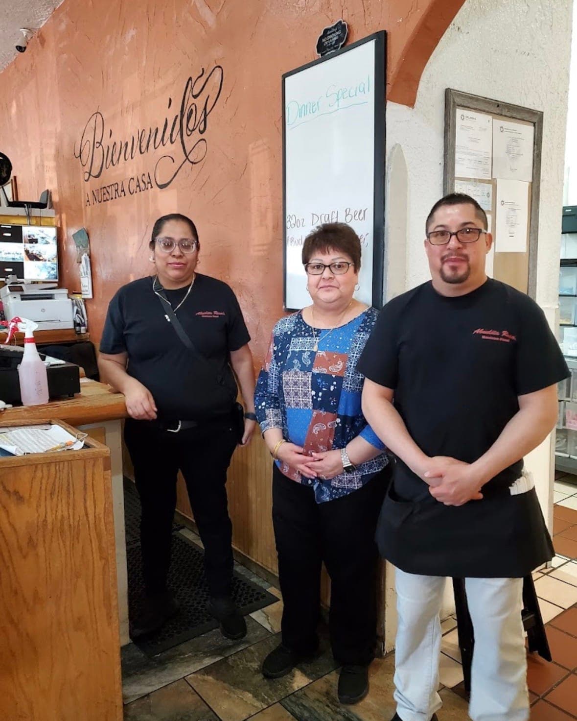 Three of the staff at Abuelita Rosa's standing together by the front counter, under “Bienvenidos a nuestra casa” painted on the wall